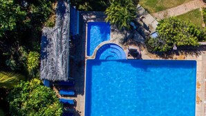 Une vue aérienne d’une piscine entourée de chaises longues et de parasols, avec une végétation luxuriante en arrière-plan.