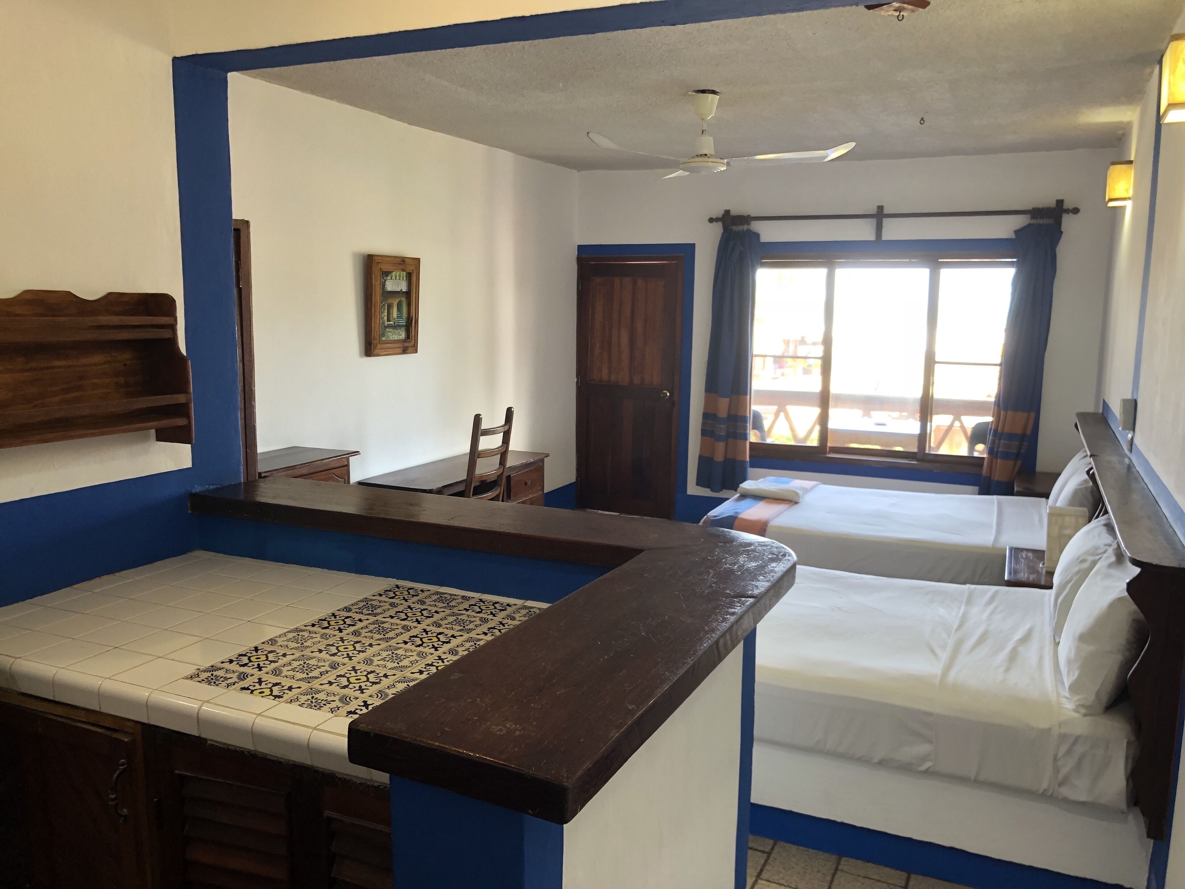 A room with a bed, a desk, a chair, a ceiling fan, and a window with curtains.