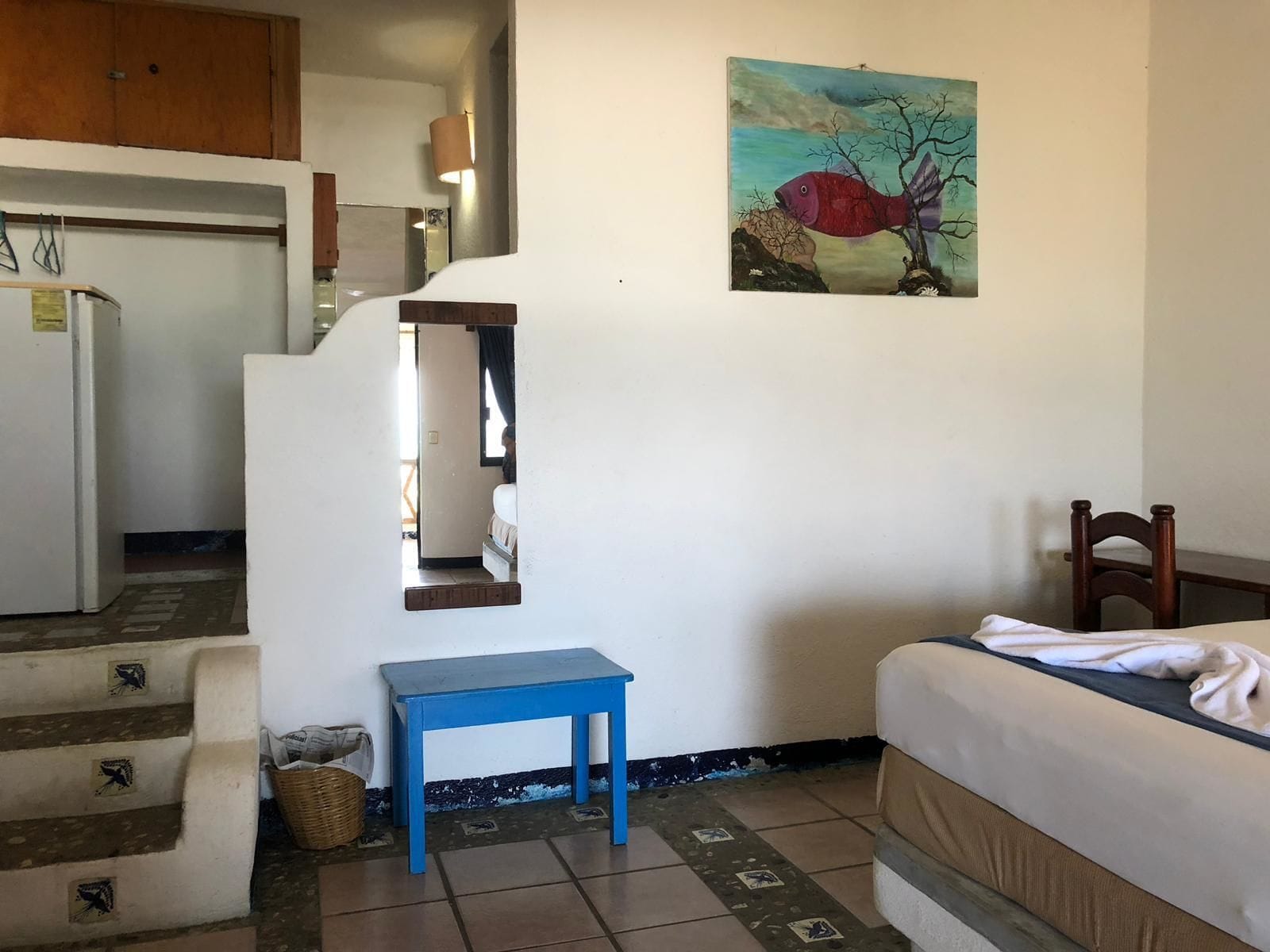 A bedroom with a bed, a blue table, a painting, and a staircase leading to a kitchen.