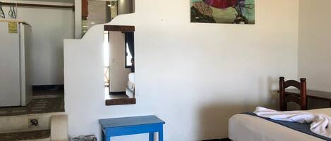 A bedroom with a bed, a blue table, a painting, and a staircase leading to a kitchen.