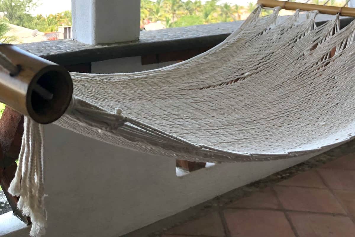 Una hamaca en un balcón con vista a la playa y al océano.