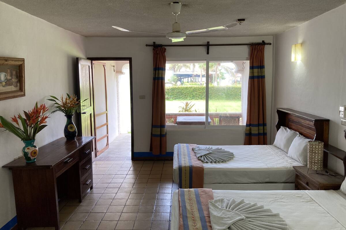 Una habitación de hotel con cama, mesitas de noche, un escritorio y una ventana con cortinas.