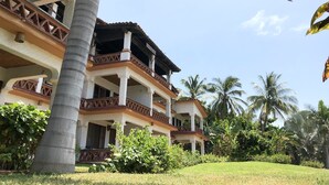 Un immeuble à plusieurs étages doté de balcons, entouré d’une végétation luxuriante et de palmiers.