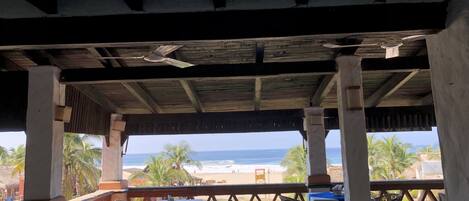 An outdoor dining area with tables and chairs, overlooking a beach and ocean.