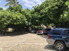 Un estacionamiento pavimentado con varios vehículos estacionados, rodeado de abundante vegetación y árboles.