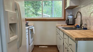 A kitchen with a window, wooden flooring, white cabinets, a stainless steel refrigerator, and a coffee maker.