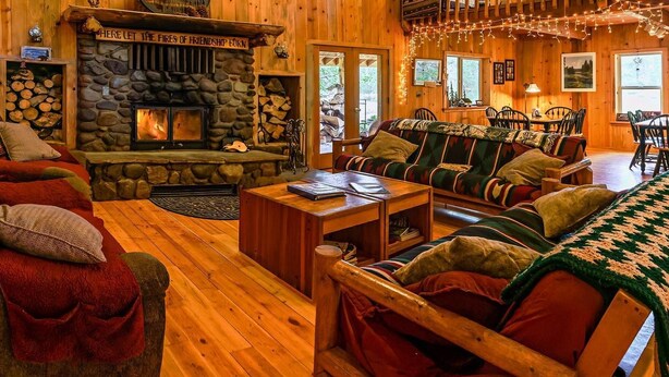 A cozy cabin interior with a stone fireplace, wooden furniture, and a dining area. - Sun Mountain Ranch Bunkhouse - Near Crater Lake (Fort Klamath)