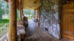 A covered porch with a stone wall and wooden door. - Sun Mountain Ranch Bunkhouse - Near Crater Lake (Fort Klamath)