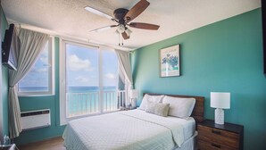 Un dormitorio con una cama grande, ventilador de techo, mesita de noche y vista al océano.