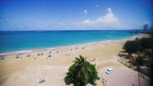 Una playa con cielo despejado, orilla arenosa y algunas sombrillas.