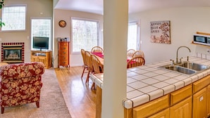A living room with a fireplace, a television, a dining area with chairs, and a kitchen with a sink and microwave. - Oak Tower Townhouse-1.5 Blocks to OSF (Ashland)