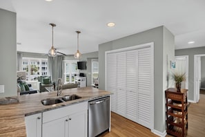 A modern kitchen with a central island, stainless steel appliances, pendant lighting, and a view of a residential area.