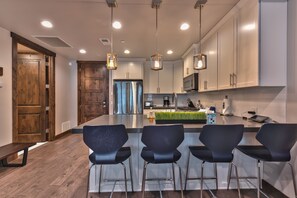 A modern kitchen with a central island, bar stools, stainless steel appliances, and pendant lighting.