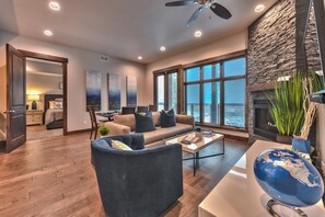A spacious living room with a large sofa, a coffee table, and a globe. There is a fireplace and a large window with a view.
