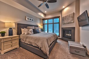 A modern bedroom with a large bed, bedside lamps, a fireplace, and a view of the outdoors.