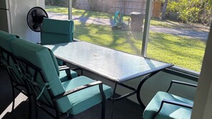 Un patio cubierto con mesa y sillas, un ventilador y vista al jardín trasero.