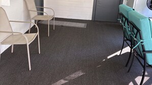 Una habitación con dos sillas, una mesita y un refrigerador. Cuenta con adornos en la pared y una puerta con ventanal.
