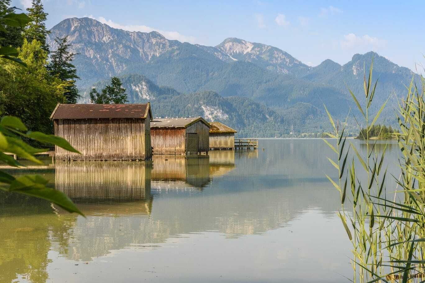 Une maison flottante en bois sur un lac paisible, avec des montagnes en arrière-plan.