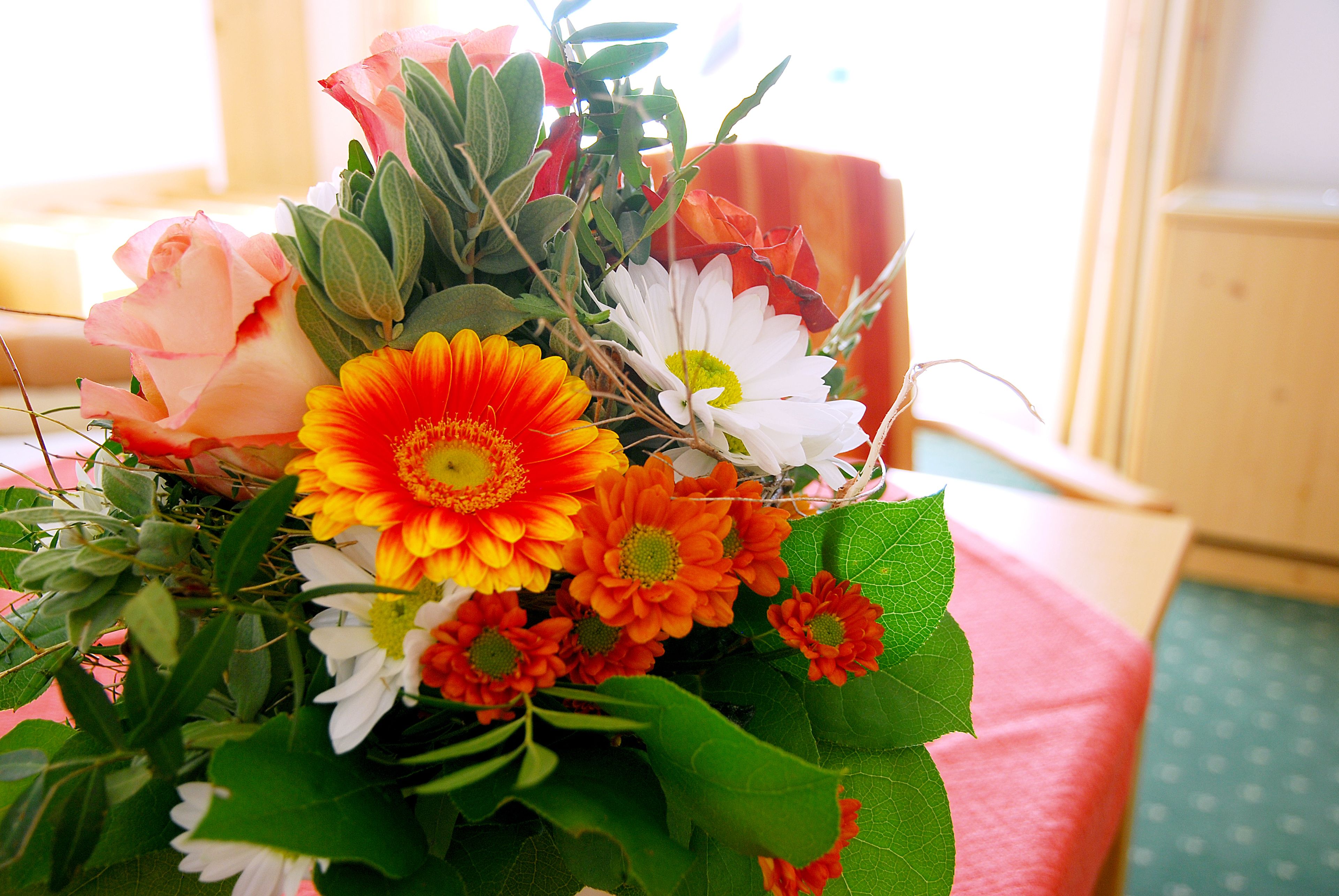 A bouquet of flowers with various colors and types, including roses and daisies, placed on a table.
