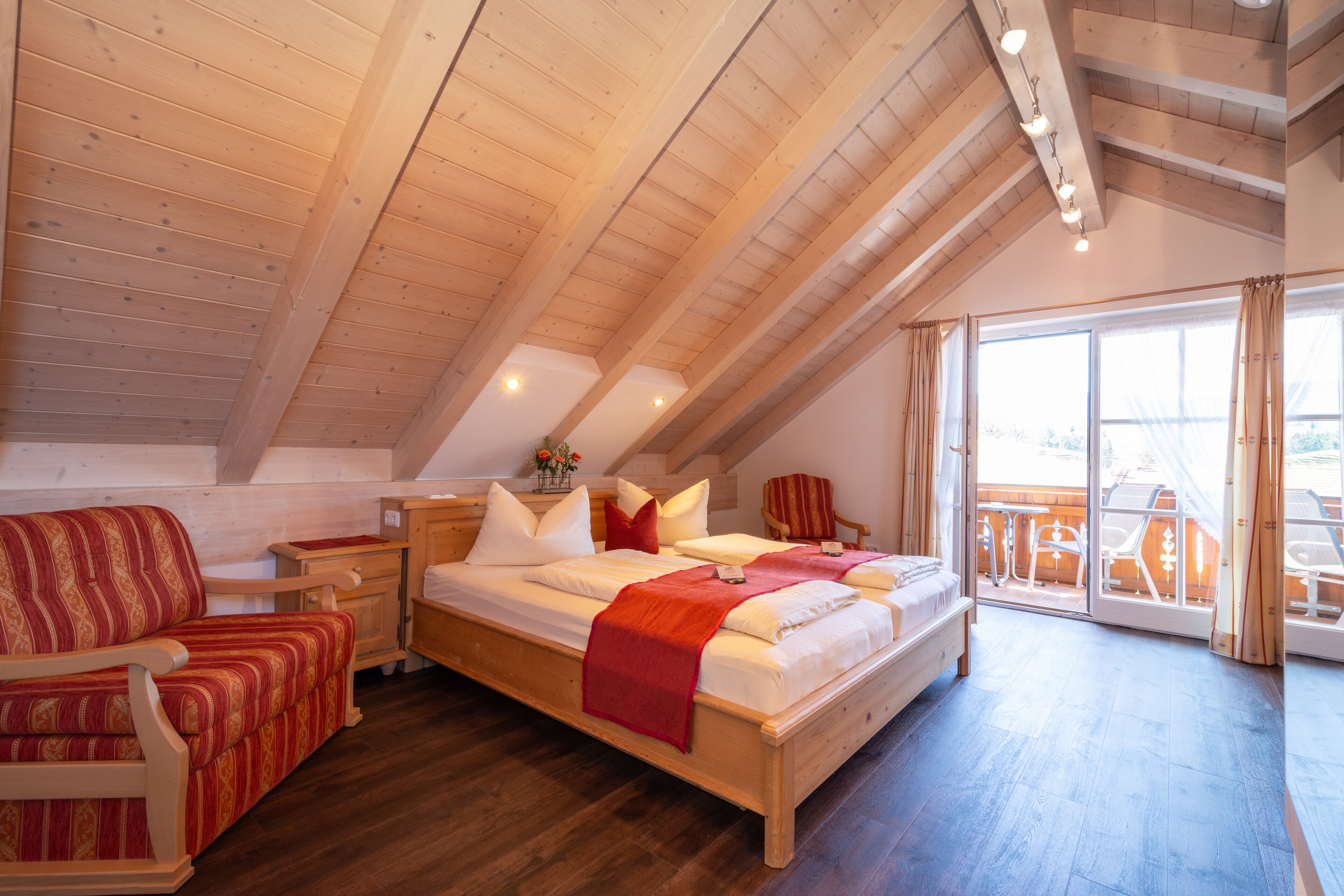 A spacious room with a large bed, a wooden ceiling, and a balcony with outdoor furniture.