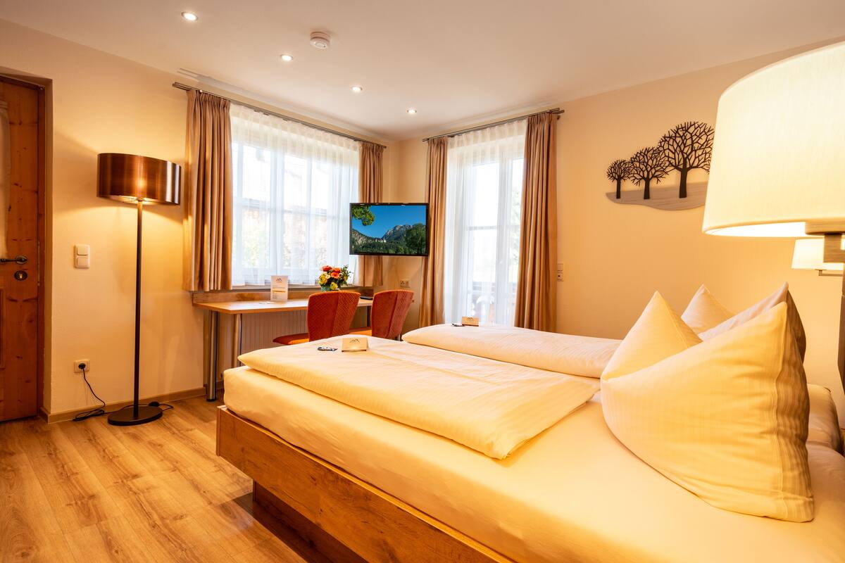 A hotel room with a bed, a desk, a chair, a TV, and a lamp.