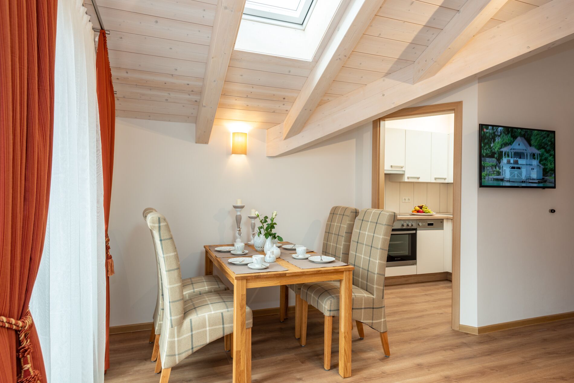 Un coin repas avec une table en bois, deux chaises, une lampe fixée au mur et, au fond, une cuisine.