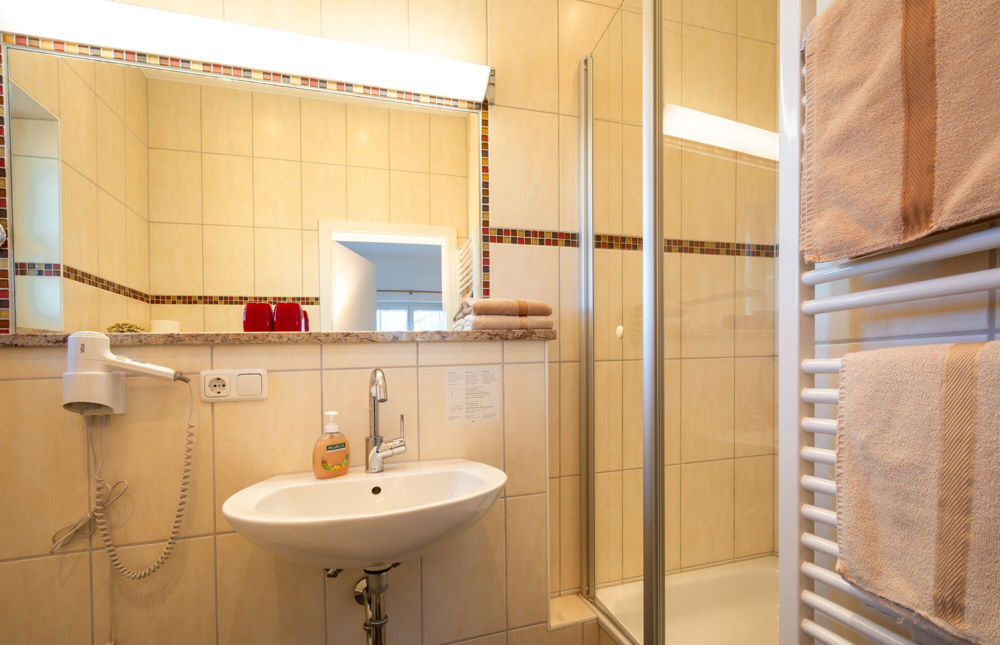 A bathroom with a sink, mirror, and shower area.