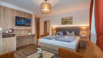 A modern hotel room with a bed, a desk, a TV, and a painting on the wall.