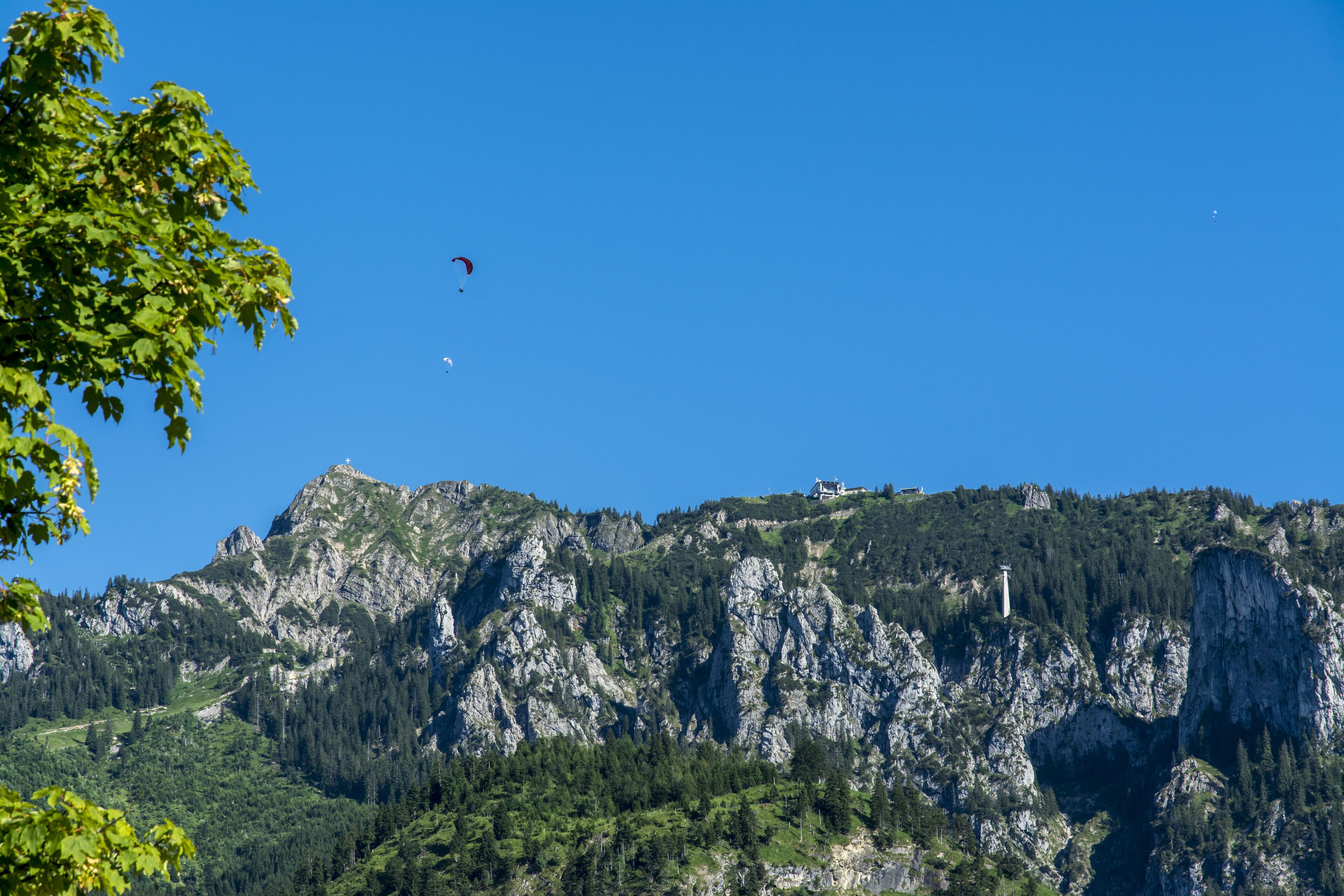 Un paisaje montañoso con cielo despejado, un edificio en la cima y una persona haciendo paracaidismo.