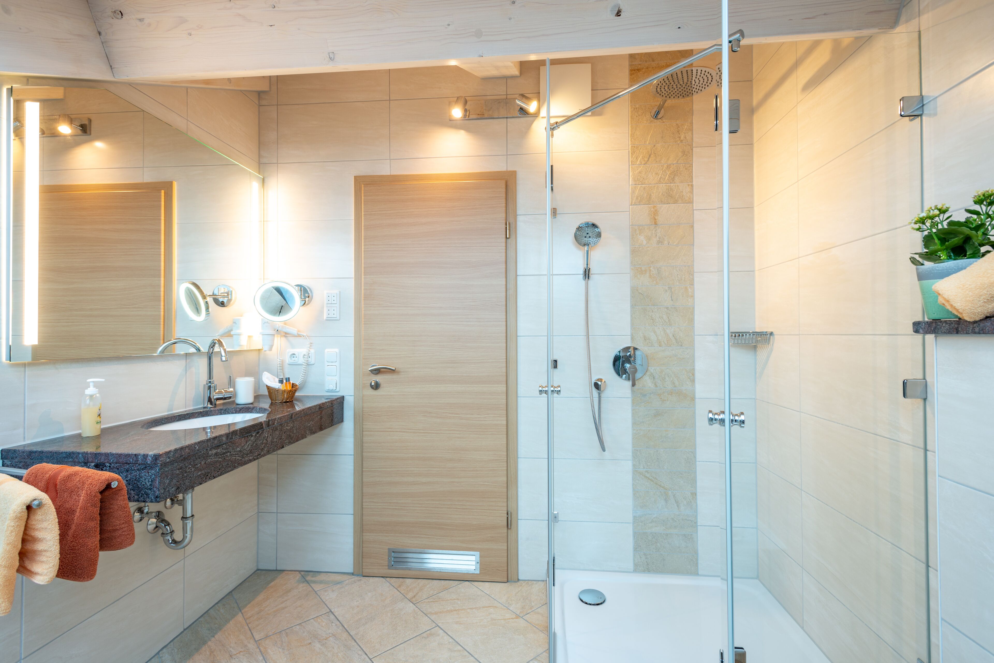 Une salle de bain moderne avec une douche à parois de verre, un lavabo doté d’un plan de travail en marbre et une porte en bois.