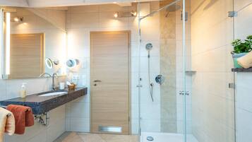 Une salle de bain moderne avec une douche à parois de verre, un lavabo doté d’un plan de travail en marbre et une porte en bois.