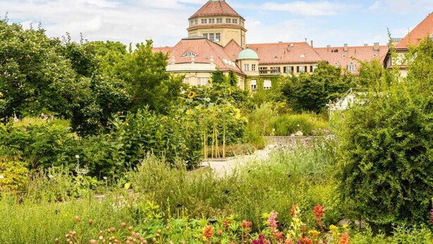 A historic building with a central tower and surrounding lush gardens.