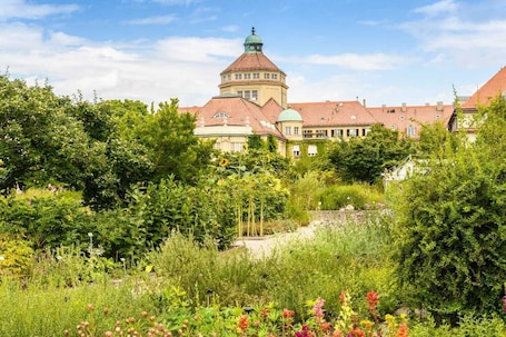 A historic building with a central tower and surrounding lush gardens.