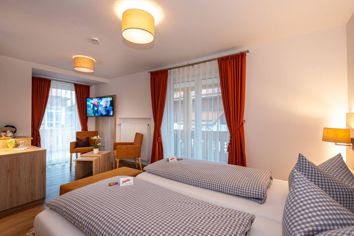 A hotel room with two beds, a desk, a chair, a television, and a window with curtains.