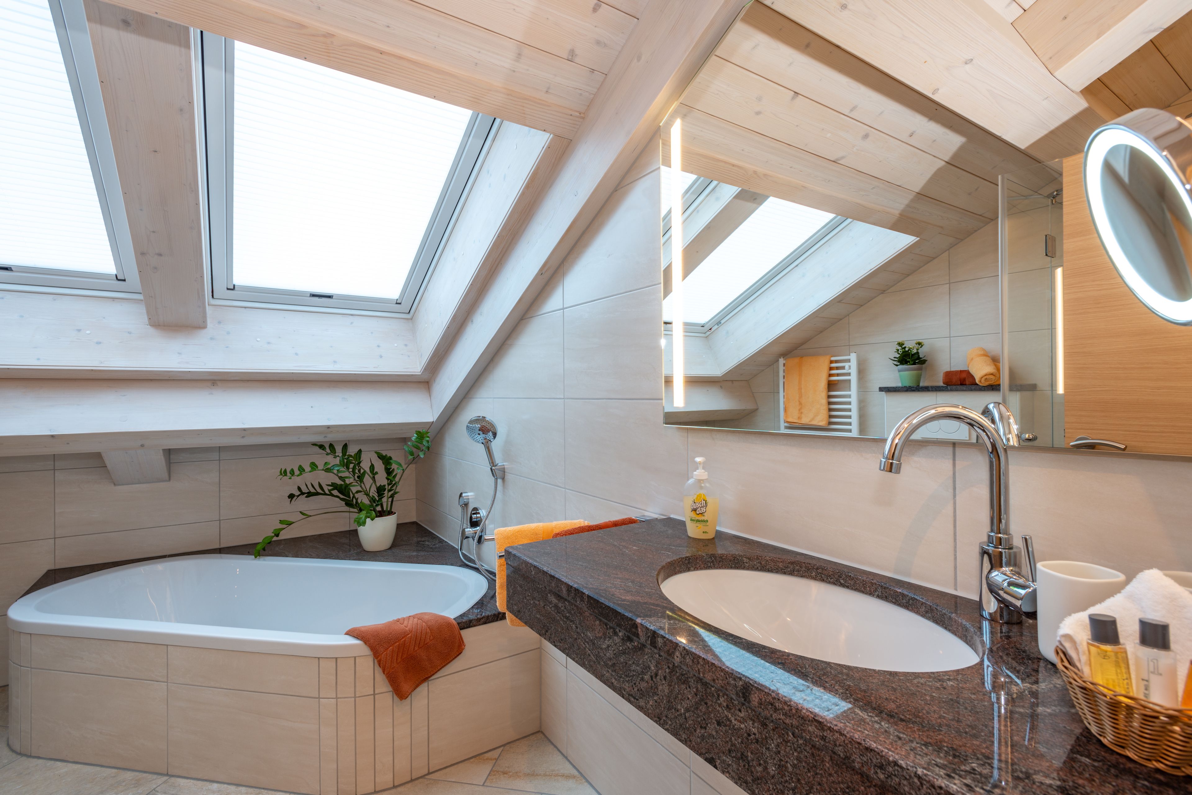Ein modernes Badezimmer mit Dachfenstern, einer freistehenden Badewanne, einem Waschbecken und einem großen Spiegel.