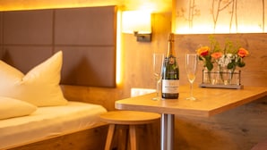 A wooden table with a bottle of Brut Dargente wine, two glasses, and a vase with flowers in a hotel room.