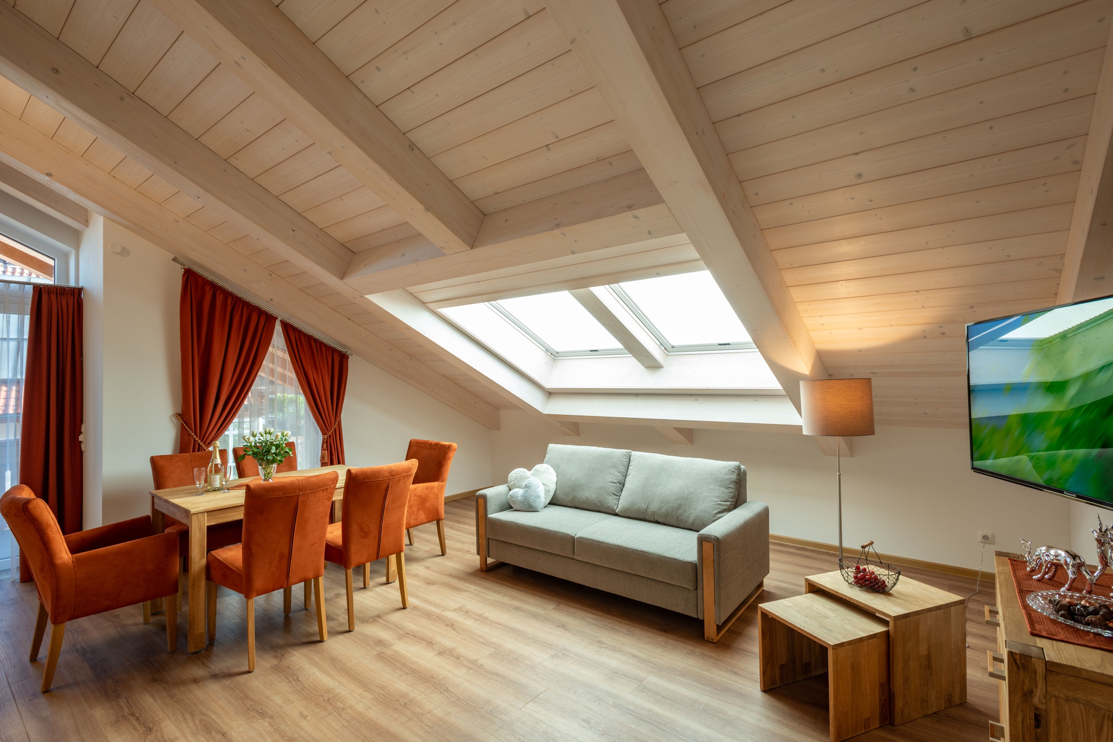Eine moderne Loft-Wohnung mit hohen Decken, Dachfenstern, einem Essbereich mit orangefarbenen Stühlen, einer Couch und einem Fernseher.