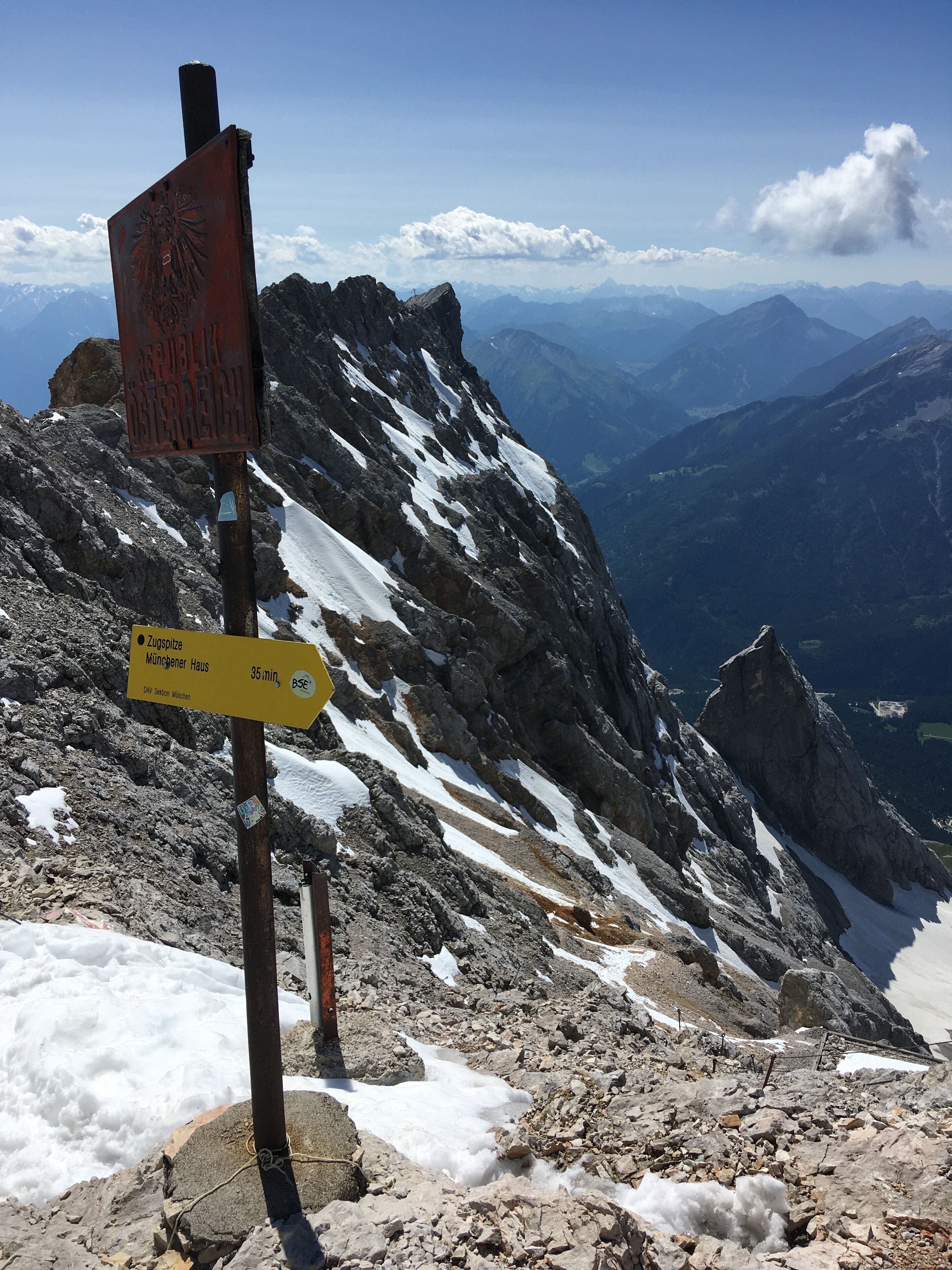 A mountain trail sign with a yellow directional sign indicating Zugspitze and Mönchener Haus, 35 minutes away, BSE.