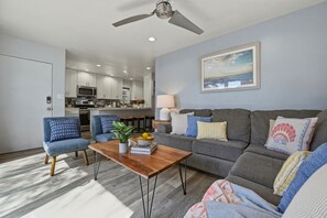 A modern living room with a grey sofa, blue armchairs, a wooden coffee table, and a ceiling fan.