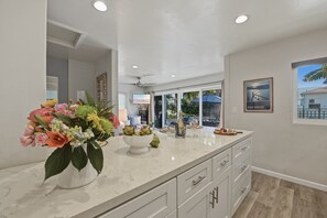 A modern kitchen with a marble countertop, white cabinetry, and a large window with a view of palm trees.