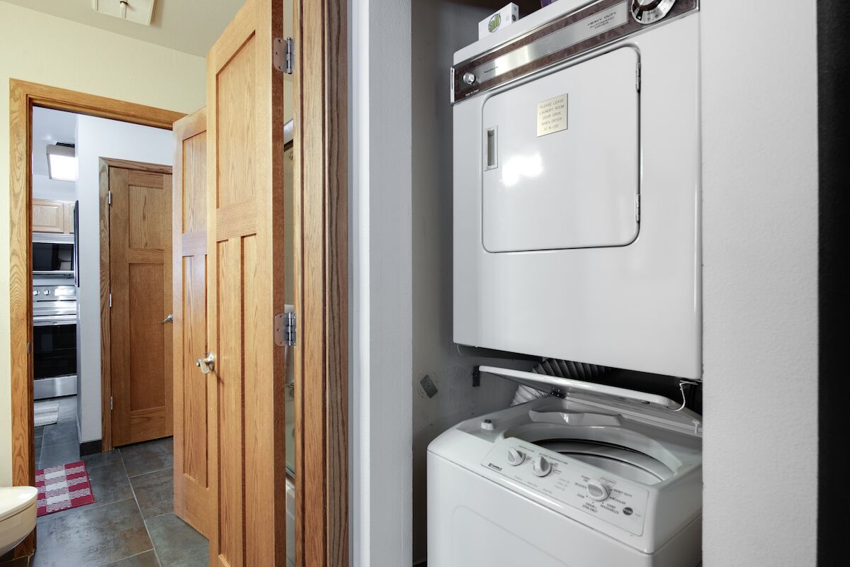 A laundry room with a front-loading washing machine and dryer, wooden doors, and a tiled floor.