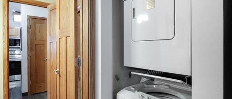 A laundry room with a front-loading washing machine and dryer, wooden doors, and a tiled floor.