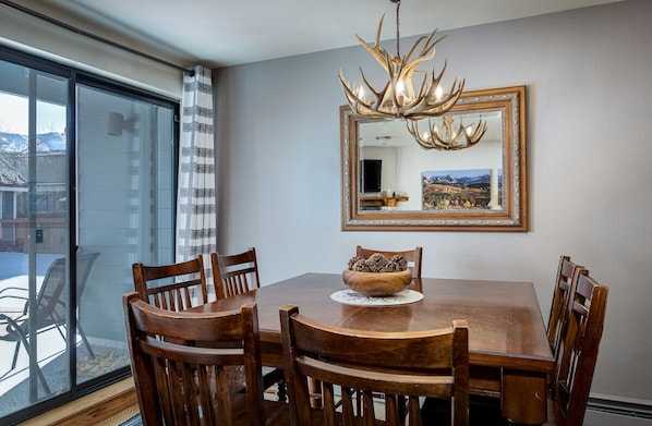 Un coin repas avec une table en bois, des chaises, un lustre et un grand miroir au mur.