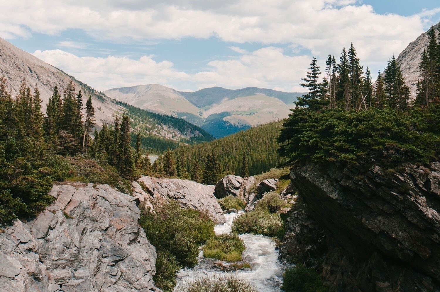 Un paysage montagneux, traversé par une rivière qui serpente dans une vallée rocheuse, le tout entouré de forêts denses et bordé de chaînes de montagnes lointaines.