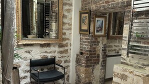 Una habitación con paredes de ladrillo visto, un espejo grande, un banco negro y un tapiz estampado.