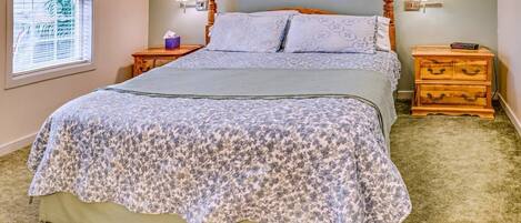 A bedroom with a large bed, two bedside tables, a nightstand, a window with blinds, and a lamp on each table.
