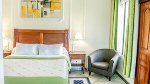 A hotel room with a bed, a chair, a nightstand, a lamp, and a window with curtains. - Tchero Hotel (Douala)