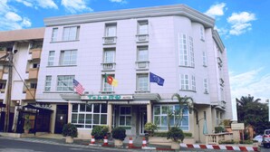 A hotel with a white facade, multiple balconies, and flags of the USA and the EU. - Tchero Hotel (Douala)