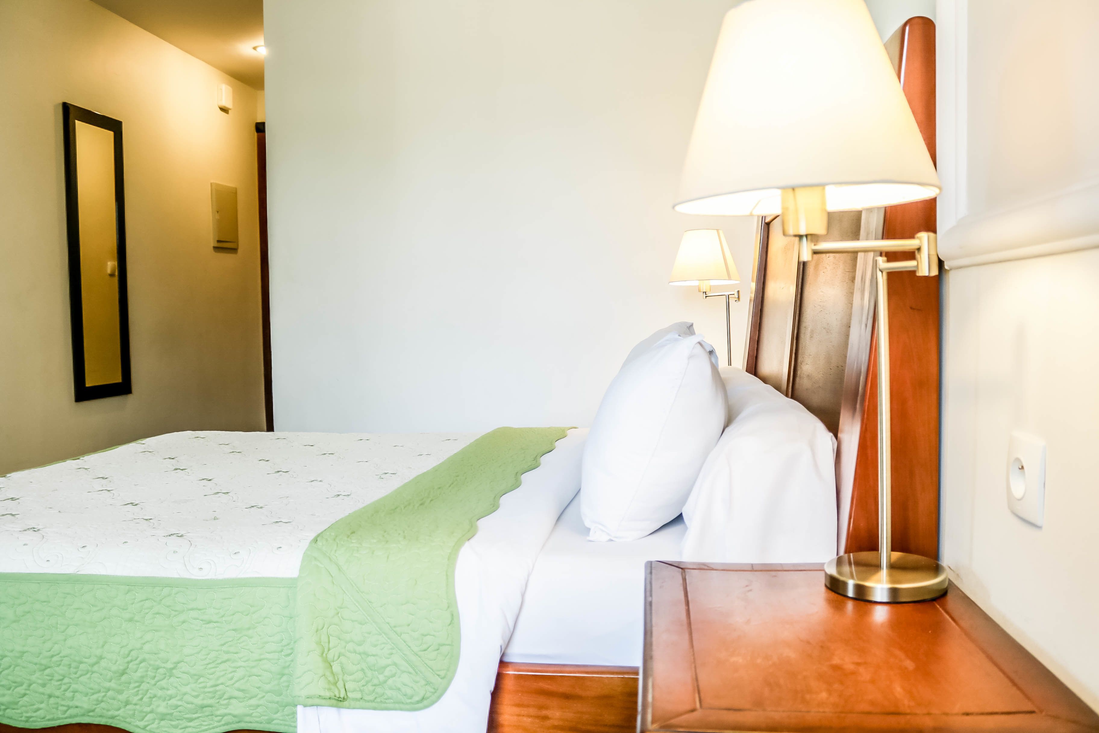 Un lit bien fait, recouvert d’une couverture verte, avec une lampe de chevet et une table de nuit en bois.