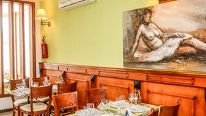 A restaurant with wooden booths and tables, a green wall, and a large painting. - Tchero Hotel (Douala)